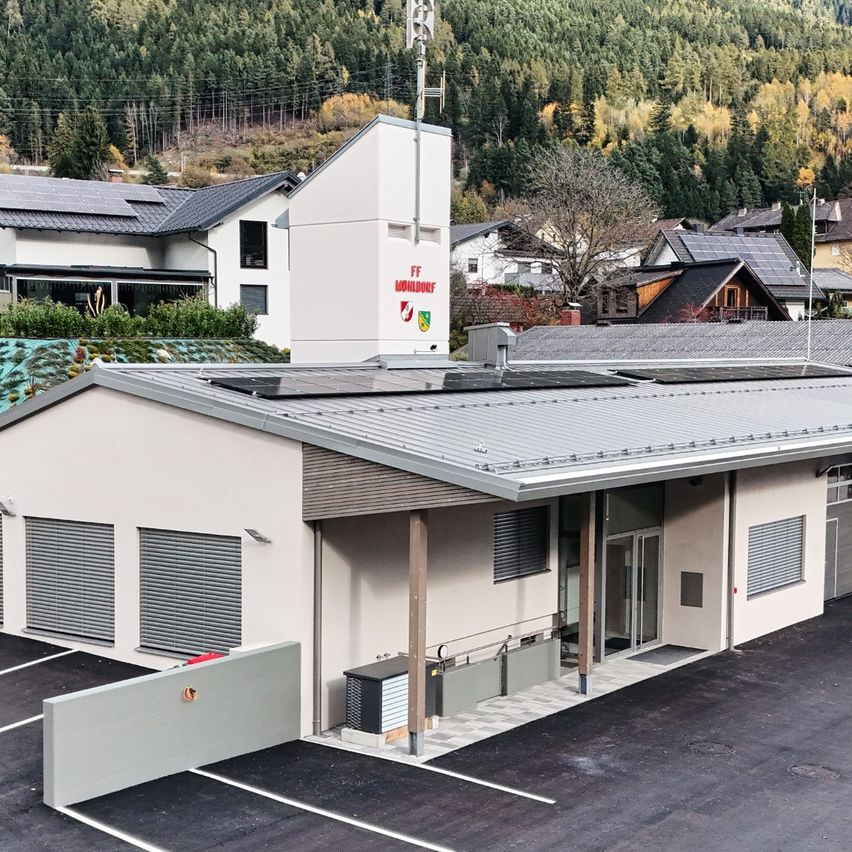Ein Luftbild einer modernen Feuerwache mit Solarmodulen auf dem Dach, umgeben von Häusern und Bergen im Hintergrund.