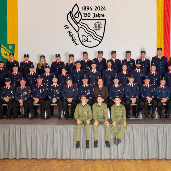 Eine Gruppe von Feuerwehrleuten in Uniform posiert für ein Foto auf einer Bühne, mit einem Hintergrund, der die Jahre 1894-2024 und 130 Jahre anzeigt.