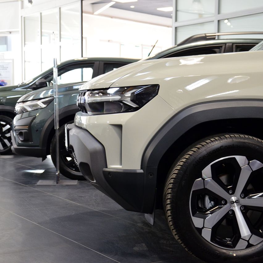 Zwei Autos sind in einem Showroom geparkt. Eines ist ein beigefarbenes Auto mit einem Logo auf dem Stößer und das andere ist ein grünes Auto.