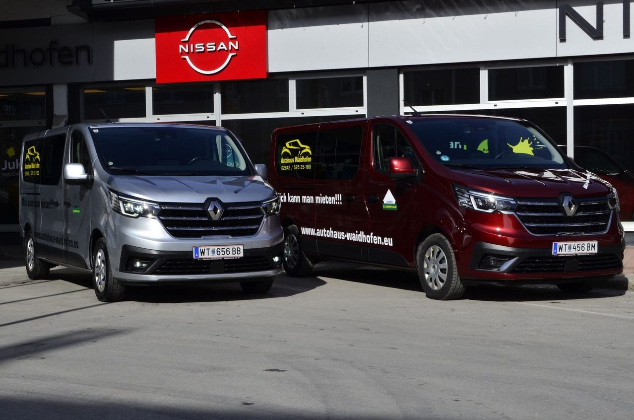 Zwei Autos sind vor einem Nissan-Händler geparkt. Ein silberner Renault und ein roter Van mit der Website www.autohaus-waldhofen.eu.