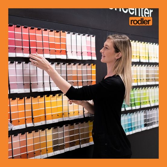 Eine Frau mit blondem Haar steht vor einer Farbkarte und wählt möglicherweise eine Farbe für ein Projekt aus.