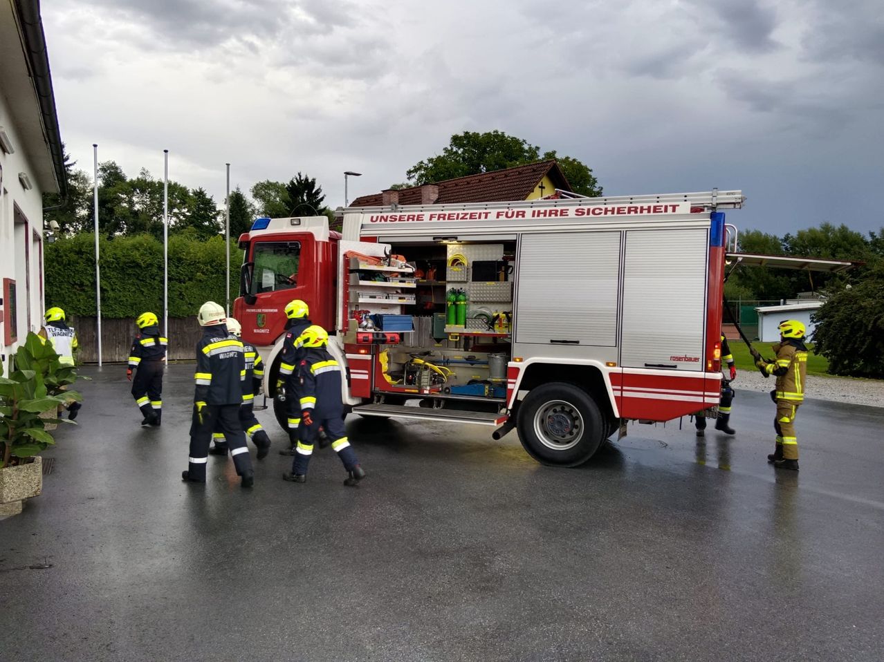 Ein Feuerwehrauto mit offenen Türen und vorbeigehenden Feuerwehrleuten. Das Auto trägt die Aufschrift 'Unsere Freiheit für Ihre Sicherheit'.
