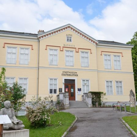 Das Alte Rathaus, ein gelbes Gebäude mit mehreren Fenstern, zeigt das Stadtmuseum Stadtbibliothek auf der Vorderseite. Vor dem Gebäude steht eine Statue, ein gepflasterter Weg führt zum Eingang.