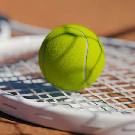 Ein Tennisschläger mit einem Tennisball darauf auf einem Tennisplatz.