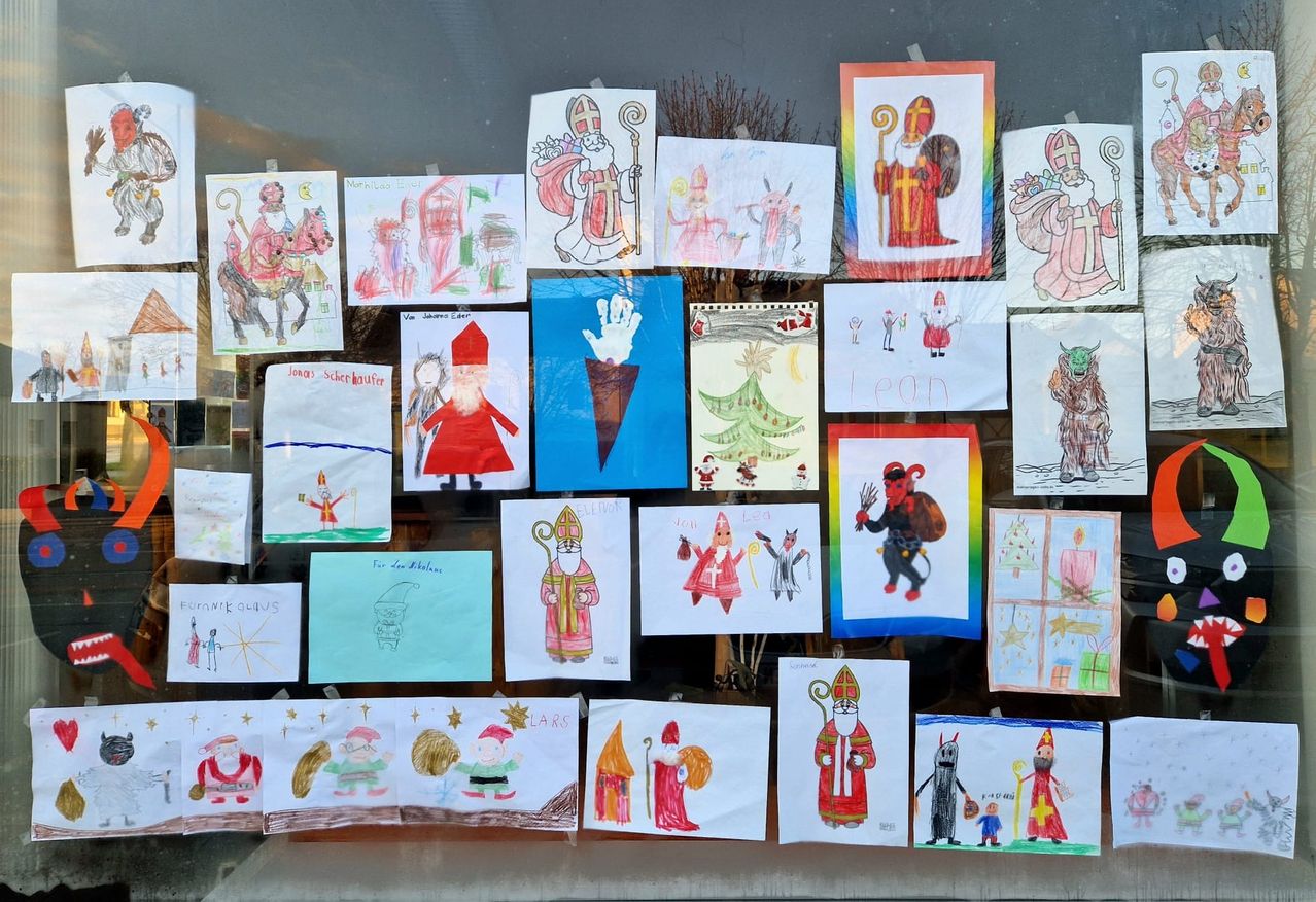 Eine Ausstellung von Kinderzeichnungen mit dem Weihnachtsmann und anderen festlichen Charakteren schmückt eine Glasoberfläche und zeigt verschiedene künstlerische Interpretationen.