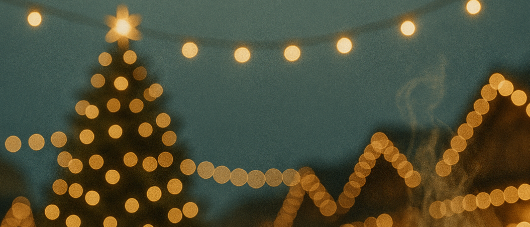 Eine Tasse Kaffee mit einem Weihnachtsmann-Design auf einem Holztisch. Im Hintergrund steht ein beleuchteter Weihnachtsbaum. Das Wort Christkindlmarkt ist prominent angezeigt.