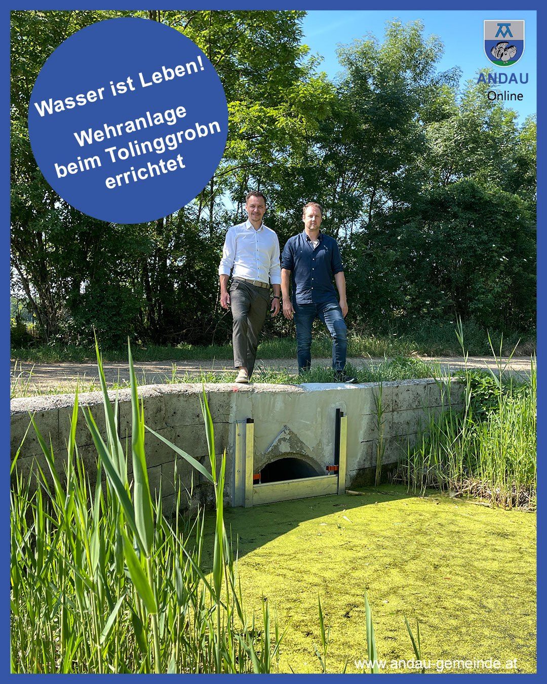 Zwei Männer stehen in der Nähe eines Entwässerungstunnels mit einem Schild, das auf Deutsch 'Wasser ist Leben' steht. Im Hintergrund sind Bäume und Gras zu sehen.