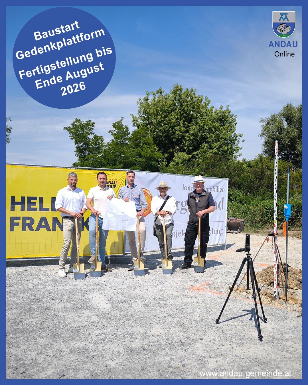 Fünf Männer in leichter Kleidung halten Schaufeln in der Hand und stehen vor einem gelben Banner, möglicherweise bei einer Grundsteinlegungszeremonie. Ein großer blauer Kreis ist überlagert auf dem Bild, mit dem Text 'Gedenkplatte Fertigstellung Ende August 2026'.