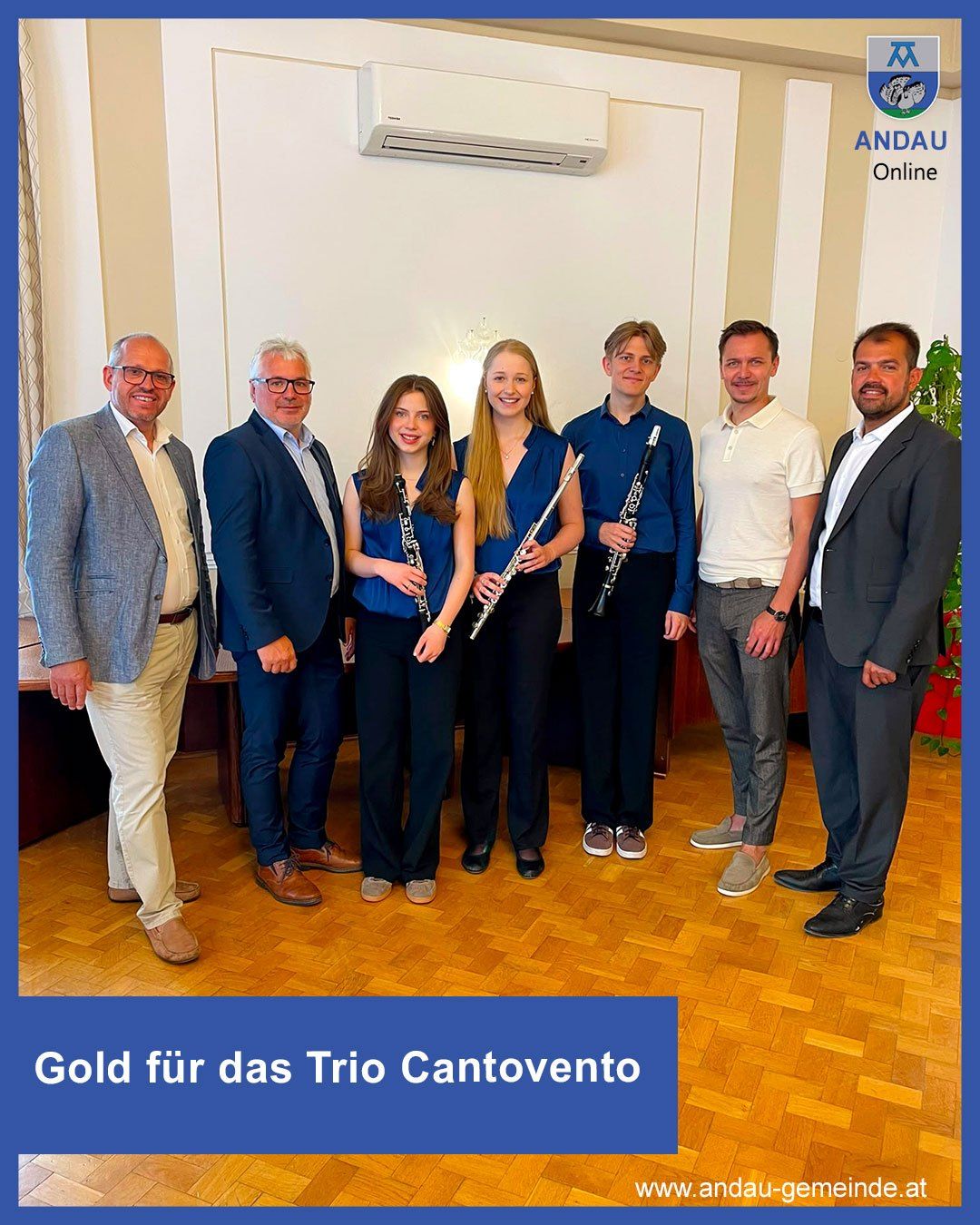 Sechs Personen posieren mit Musikinstrumenten, darunter Flöte und Klarinette, in einem Raum mit Holzboden. Der Text lautet 'Gold für das Trio Cantovento'.