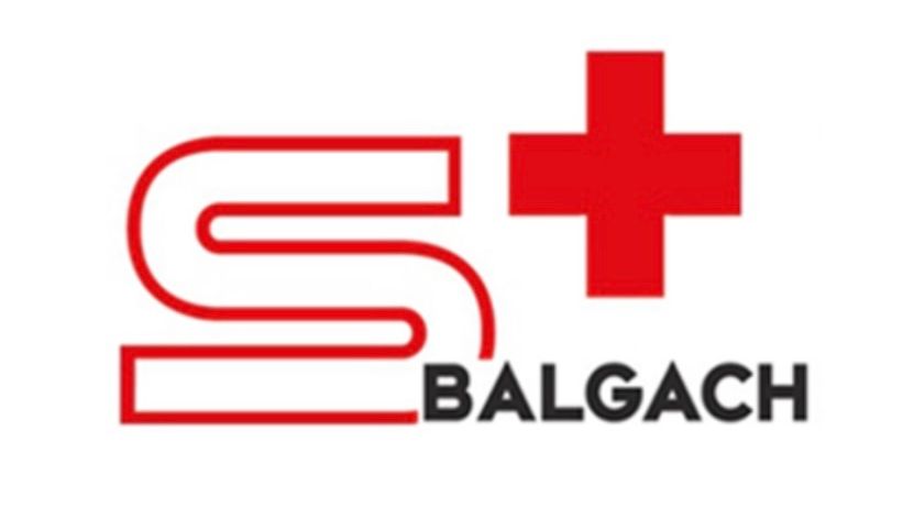 Das Logo zeigt einen stilisierten Buchstaben 'S' mit einem roten Kreuzsymbol auf der rechten Seite. Der Wort 'BALGACH' steht darunter in Schwarz geschrieben.
