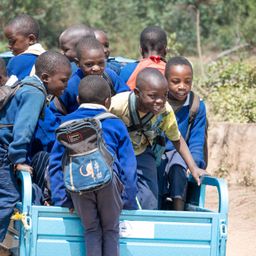 Eine Gruppe junger Jungen in blauen Uniformen fährt im Heck eines blauen Lastwagens. Einige tragen Rucksäcke.