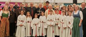 Eine Gruppe von Menschen, darunter Kinder in weißen Gewändern und Erwachsene in traditioneller Kleidung, posiert für ein Foto unter einem Zelt mit dem Schriftzug 'Leitgeb Festzeltverleih'.