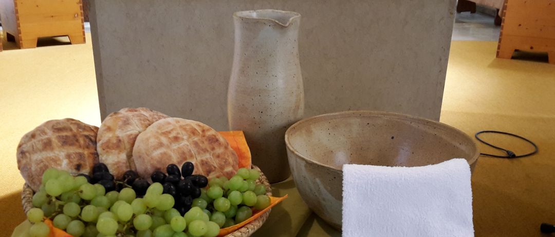 Eine Tischdekoration mit einer Schüssel Trauben, Brot und einem Krug auf einem grünen Tuch.