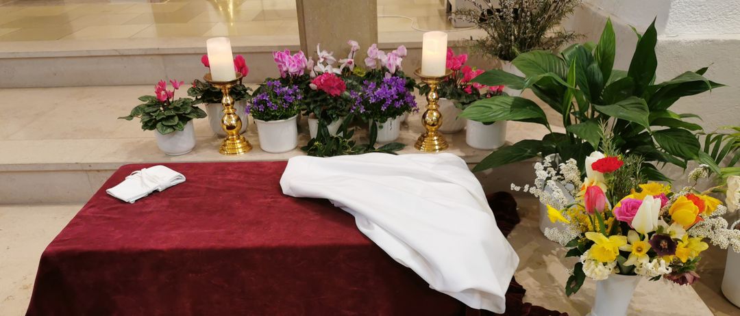 Ein marmorierter Altar mit einem weißen Tuch, Kerzen und Blumenvasen auf der Seite.