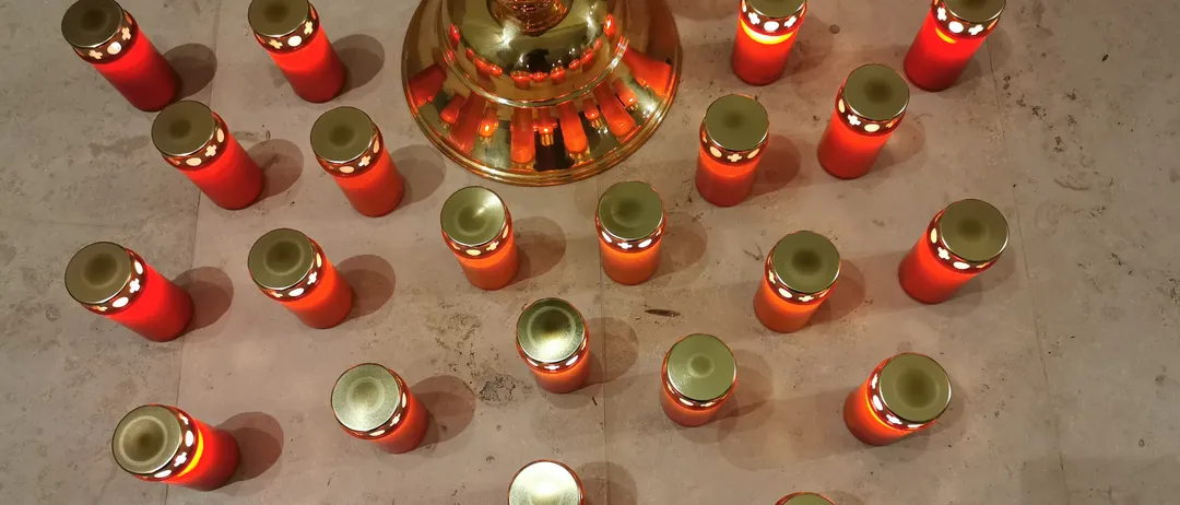 Ein Kreis roter Kerzen mit goldenen Deckeln ist auf einem gefliesten Boden angeordnet, mit einer goldenen Lampe in der Mitte.