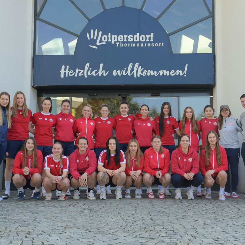 Eine Fußballmannschaft steht vor einem Gebäude. Das Schild lautet Loipersdorf Thermenresort. Die Mannschaft trägt rote Trikots.