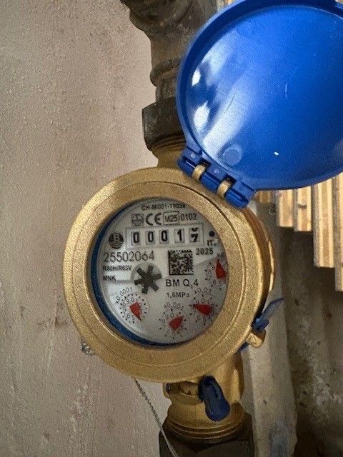 Das Bild zeigt einen Wasserzähler mit einer blauen Abdeckung. Der Zähler zeigt 25502064 an. Der Zähler hat ein rotes Sternsymbol und einen QR-Code mit dem Text BM Q.4.