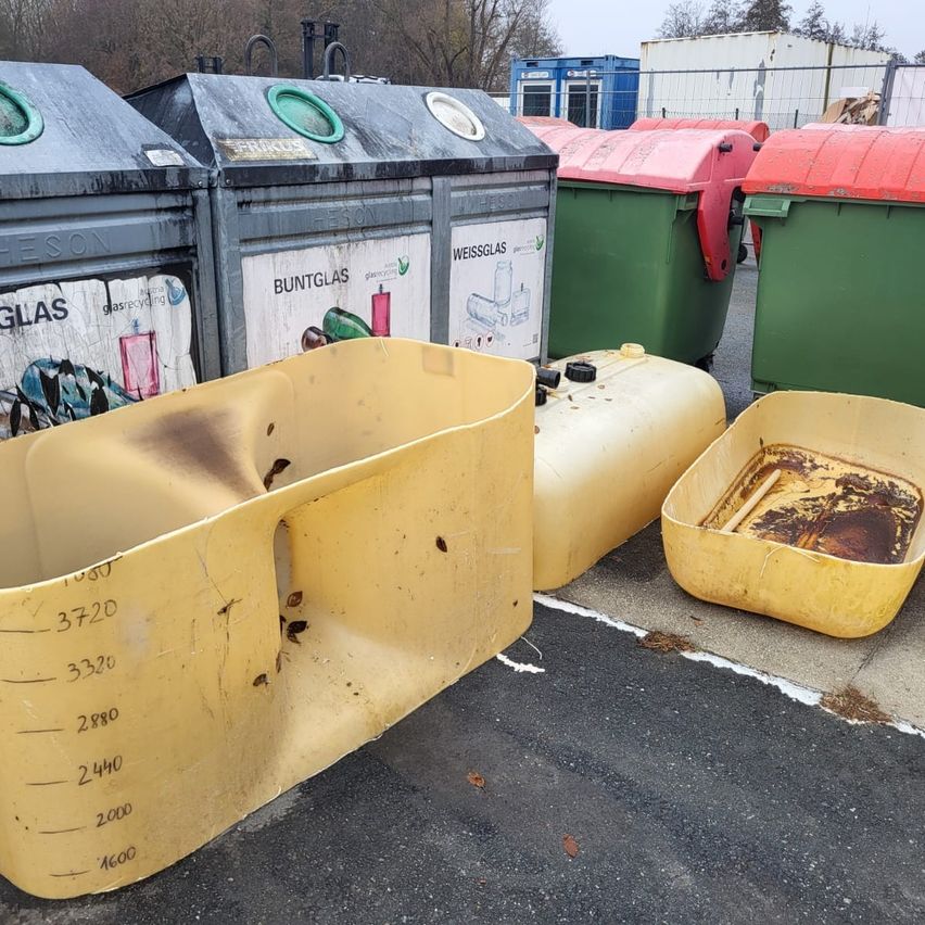 Eine Sammlung gelber Behälter mit Maßen und Markierungen steht draußen mit verschiedenen farbigen Recyclingbehältern im Hintergrund.