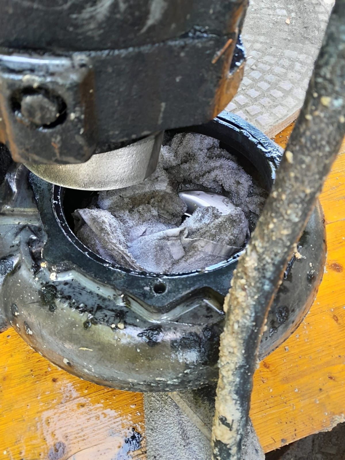 Eine Nahaufnahme eines schmutzigen, verrosteten Maschinenteils mit Schmutz und einem zerbrochenen Metallstück im Inneren. Das Teil liegt auf einer Holzoberfläche.