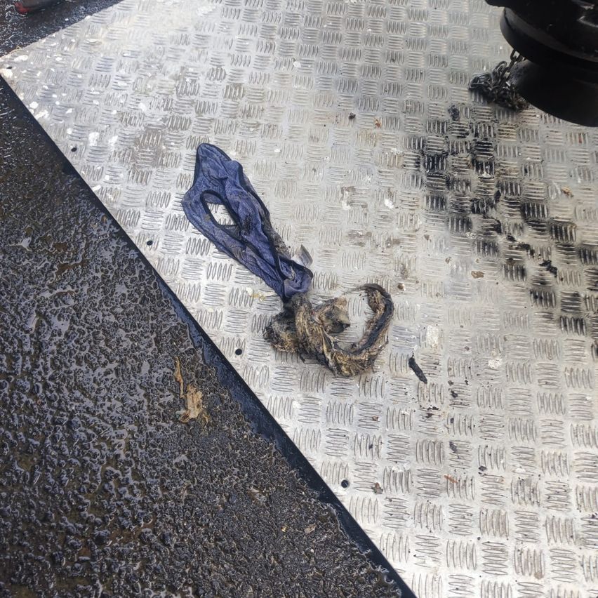 Ein zerrissenes Stück blauen Stoffes liegt auf einem Metallboden mit einer Kette und einigen schwarzen Flecken.