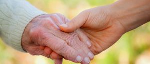 Die faltige Hand eines älteren Menschen hält die Hand eines Jüngeren, was Unterstützung und Verbindung symbolisiert.