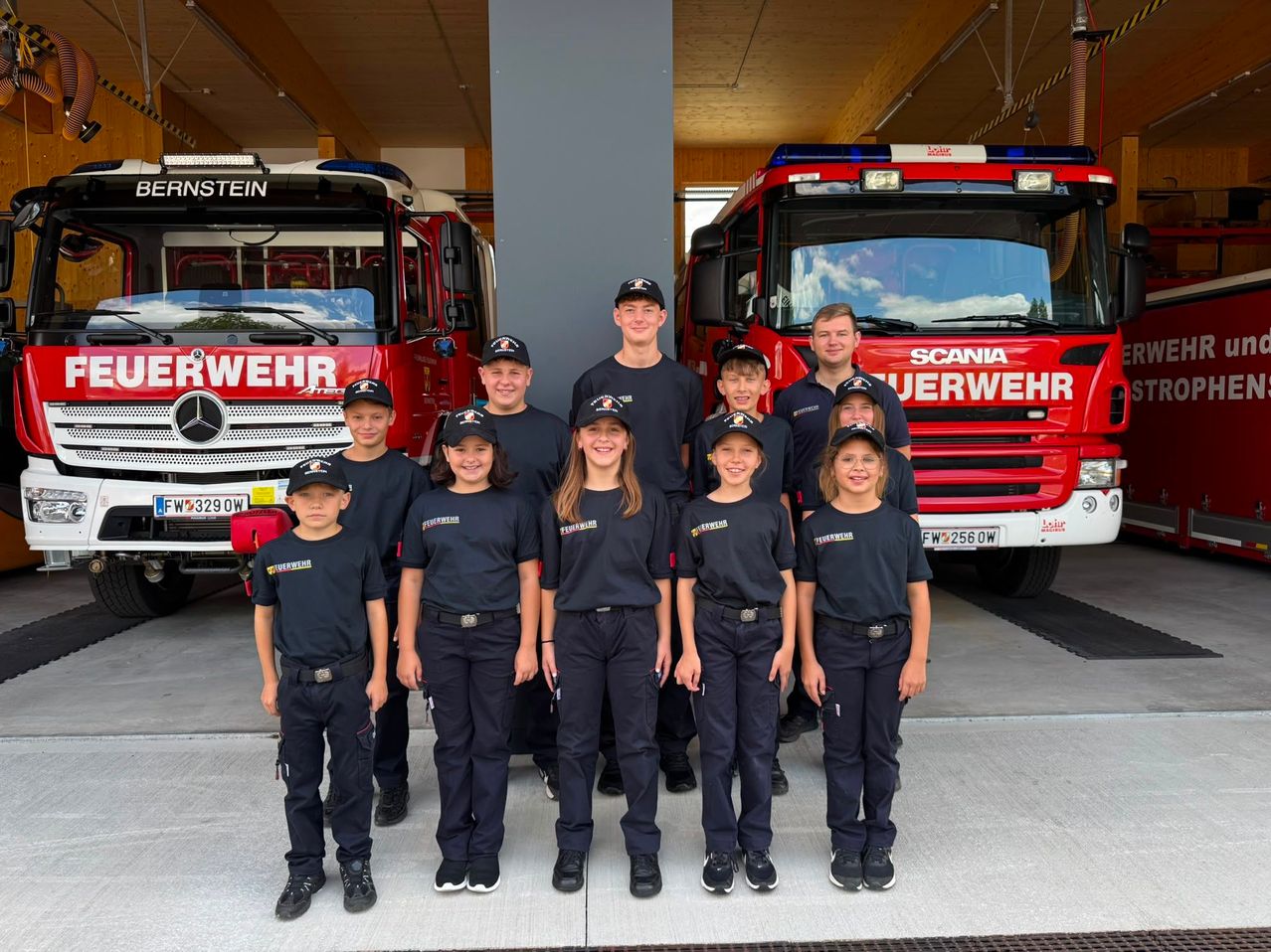 A group of children dressed in firefighter uniforms pose for a photo in front of two fire trucks.