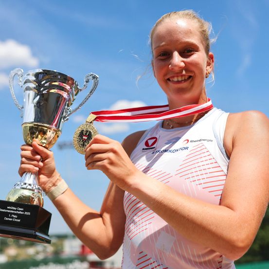 Eine Frau hält eine Goldmedaille und einen Pokal mit dem Wort Stromkontor darauf. Der Pokal steht für win2day Open Dameneinzel 2025.