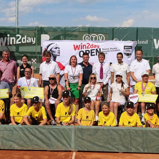 Eine Gruppe von Tennisspielern, sowohl stehend als auch sitzend in Rollstühlen, posiert für ein Foto auf einem Tennisplatz mit einem Banner, das win2day OPEN im Hintergrund zeigt.