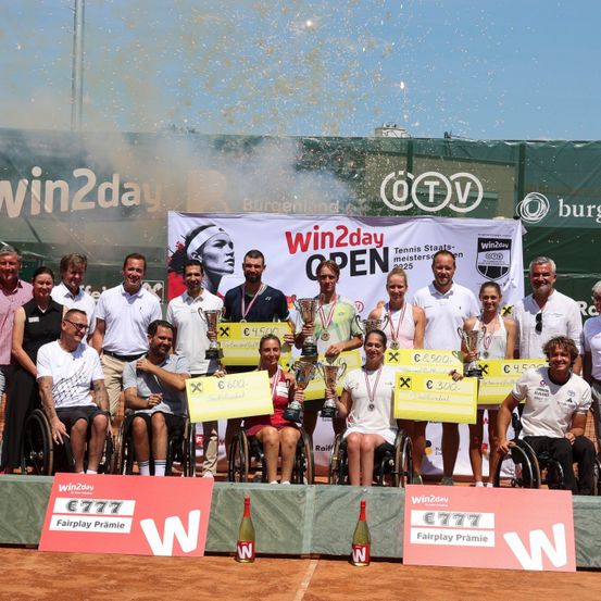 Gewinner des Win2Day Open Rollstuhltennisturniers posieren mit Trophäen und Preisgeldschecks für ein Foto, unter einem Banner mit dem Gesicht einer Frau und dem Win2Day-Logo.