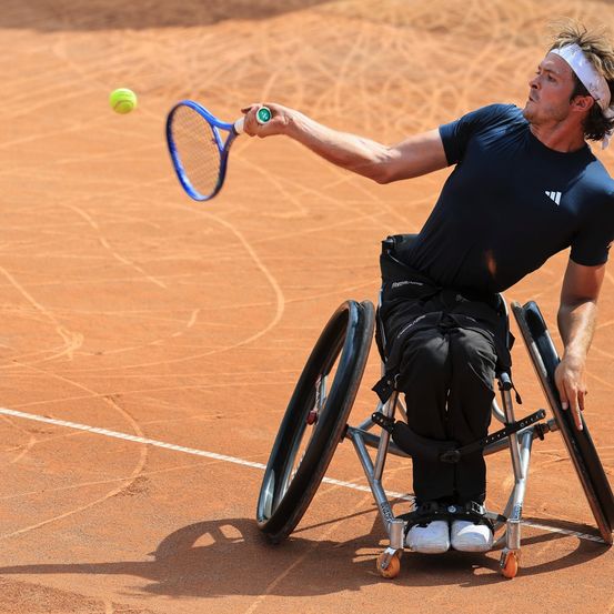 Ein Mann im Rollstuhl schwingt einen Tennisschläger, um einen Ball auf einem Tennisplatz zu schlagen.