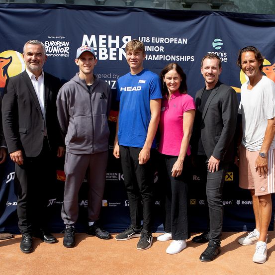 Eine Gruppe von Personen steht vor einem Banner für die U18 European Junior Championships und lächelt für ein Foto.