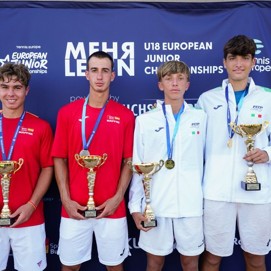 Vier junge Männer stehen nebeneinander, halten Pokale und Medaillen in der Hand, vor einem Banner für die U18 European Junior Championships.