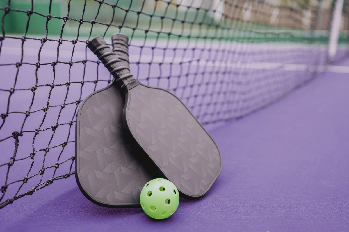 Zwei schwarze Schläger mit einem grünen Ball mit Löchern auf einer lila Oberfläche mit einem schwarzen Netz.