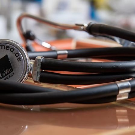 Ein Kawe-Stethoskop liegt auf einer braunen Oberfläche. Das Stethoskop hat eine silberne und schwarze Farbe mit dem Kawe-Logo auf dem Diaphragma. Der Hintergrund ist unscharf.