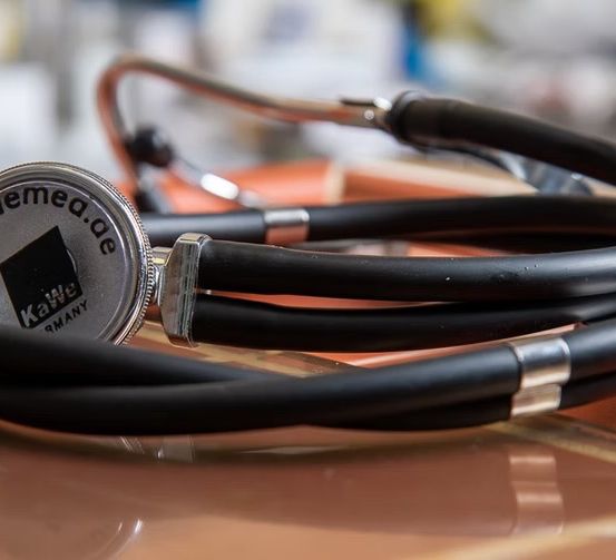 Ein Kawe-Stethoskop liegt auf einer braunen Oberfläche. Das Stethoskop hat eine silberne und schwarze Farbe mit dem Kawe-Logo auf dem Diaphragma. Der Hintergrund ist unscharf.