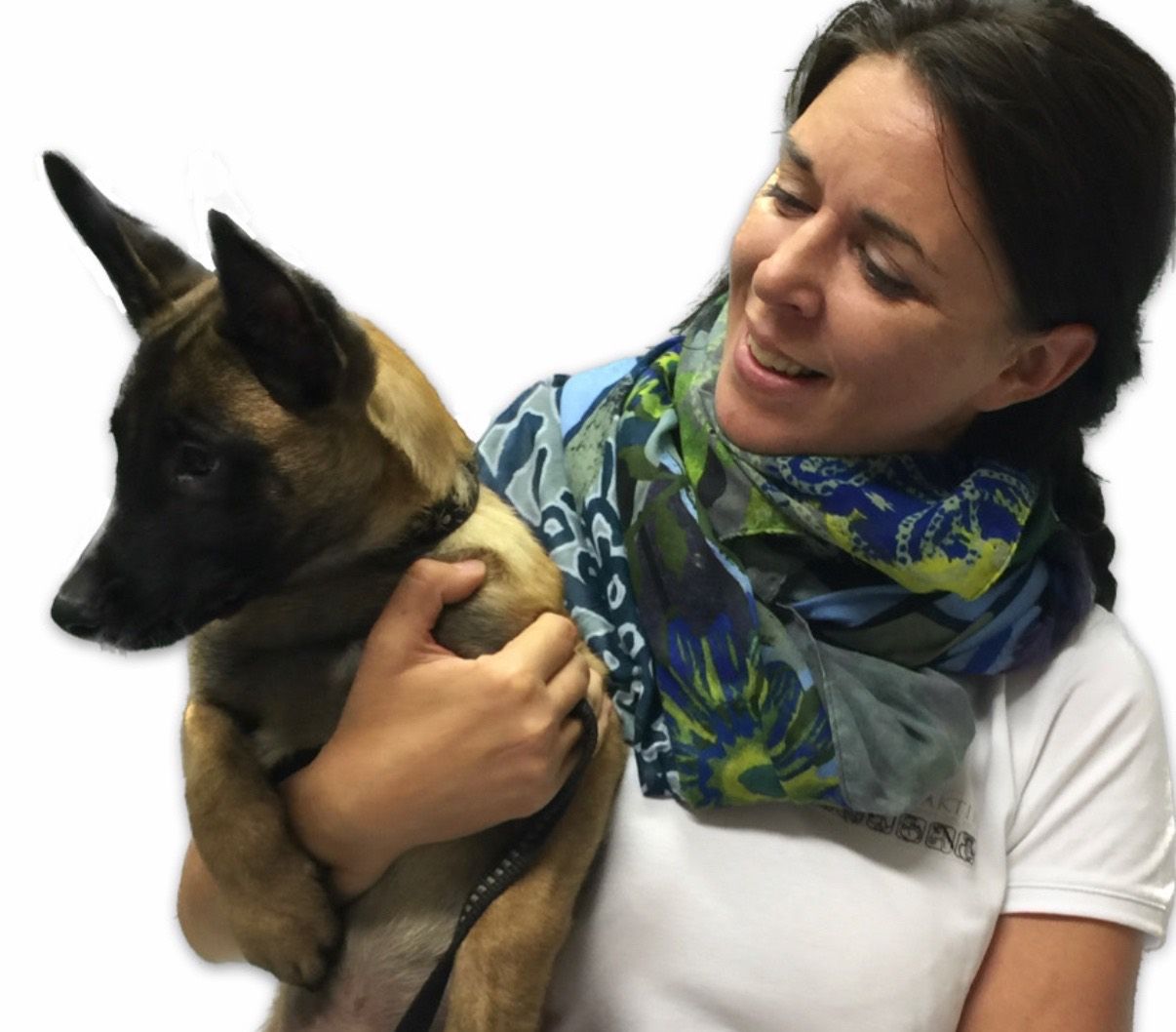 Eine lächelnde Frau mit einem Schal hält einen jungen belgischen Malinois-Hund. Der Hund schaut zu ihr auf.