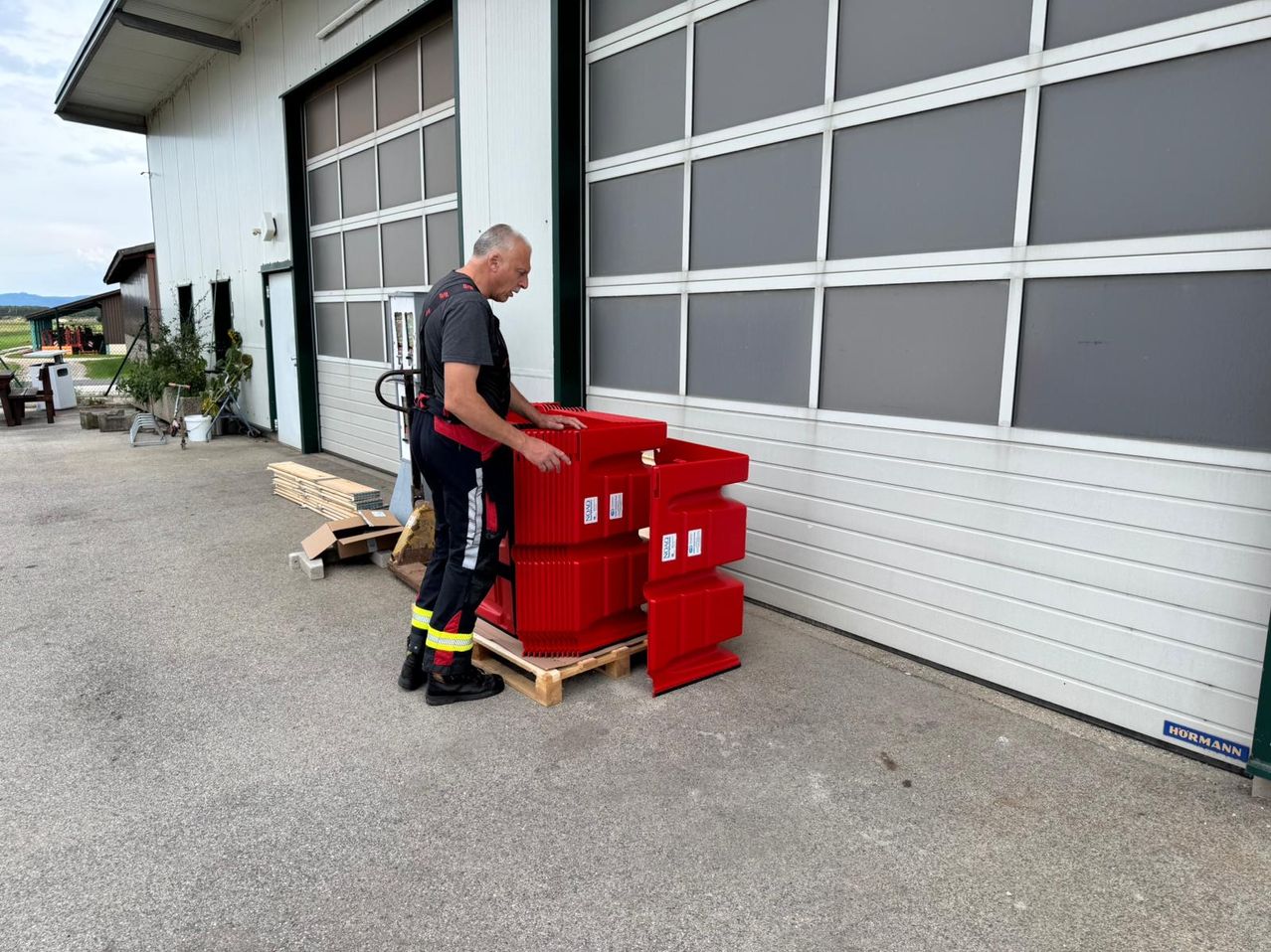Ein Mann in Schutzkleidung hebt rote Container vor einer Lagerhallengarage.