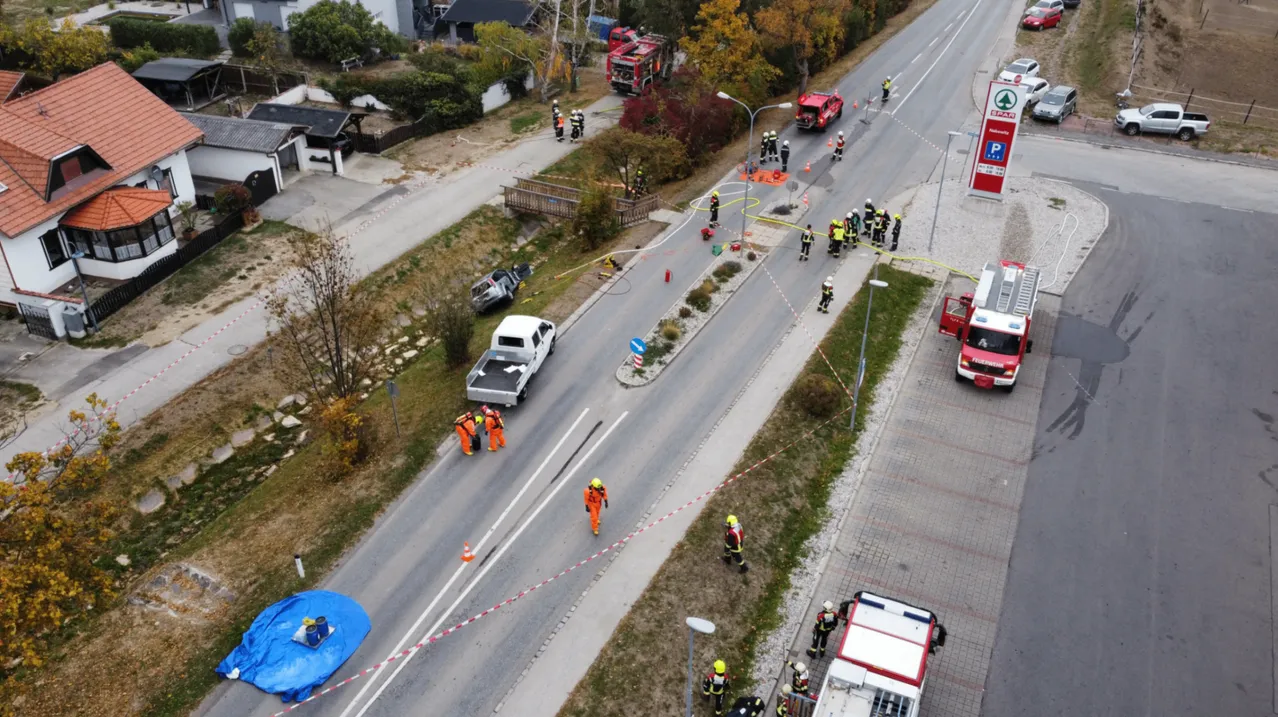 Eine Luftaufnahme einer Unfallstelle auf der Straße mit Rettungsfahrzeugen, Feuerwehrleuten und einem beschädigten Fahrzeug.