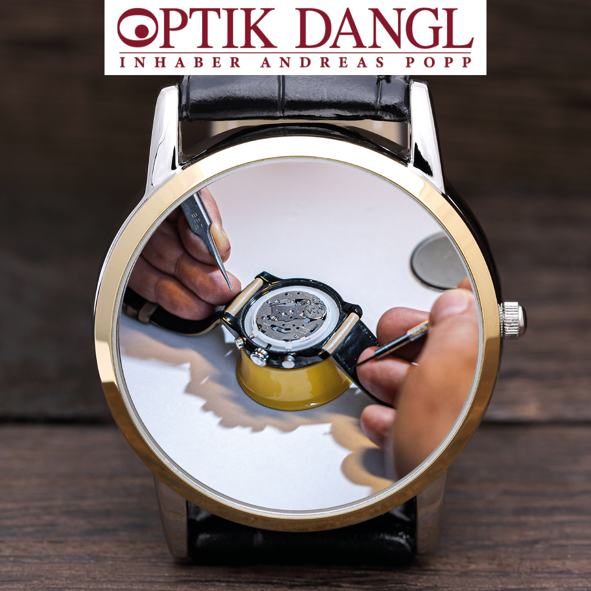 A watch is being repaired by a person holding a tool. The watch is placed on a wooden surface. The brand name is Optik Dangl.