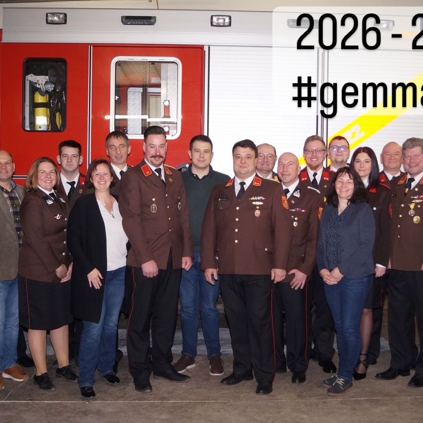 Eine Gruppe von Menschen in Uniformen und Anzügen posiert für ein Foto vor einem Feuerwehrauto mit 2026-2 darauf geschrieben.