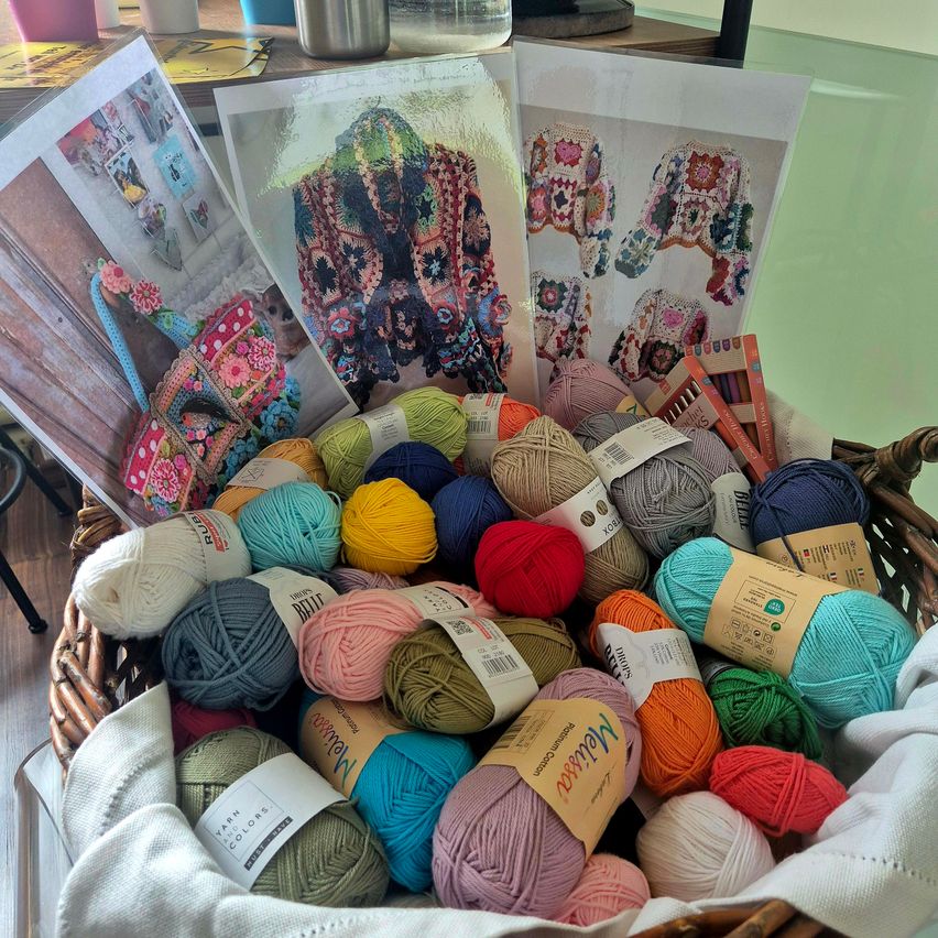 Ein Korb voller verschiedenfarbiger Garnrollen, ein Häkelmuster und ein gehäkeltes Tuch.