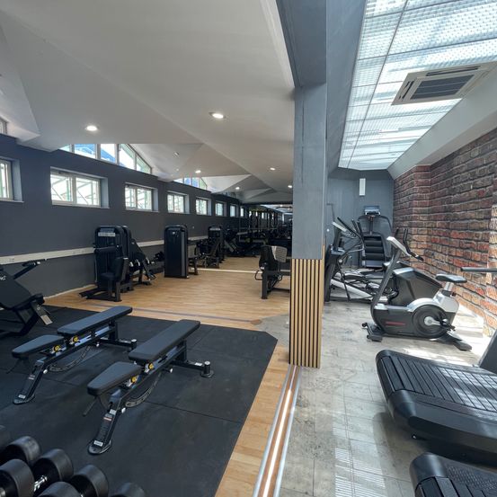 Das Innere eines modernen Fitnessstudios mit Holzböden, Ziegelwänden und einer Vielzahl von Trainingsgeräten, darunter ein Laufband, eine Hantelbank und Hanteln.