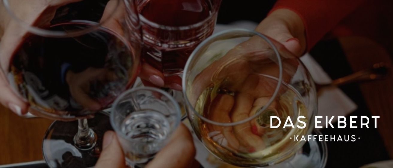 Hände halten Weingläser mit roter und klarer Flüssigkeit, reflektieren Licht, auf einer Holzoberfläche.