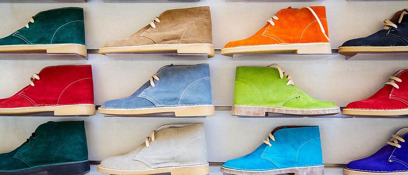 Multiple pairs of brown, blue, beige, yellow, orange, and green suede boots are displayed on a wall. The boots have different shades and are neatly arranged.