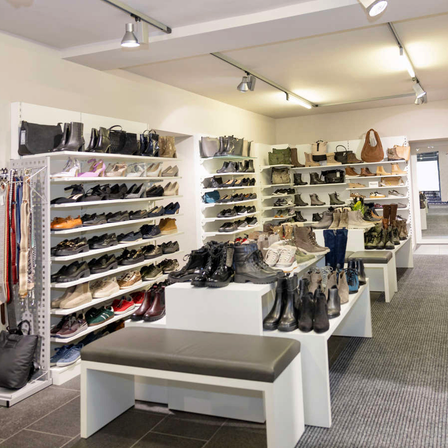 Ein Schuhgeschäft zeigt eine Vielzahl von Schuhen auf Regalen und Bänken. Der Raum ist gut beleuchtet mit Deckenleuchten und hat ein sauberes und organisiertes Erscheinungsbild.