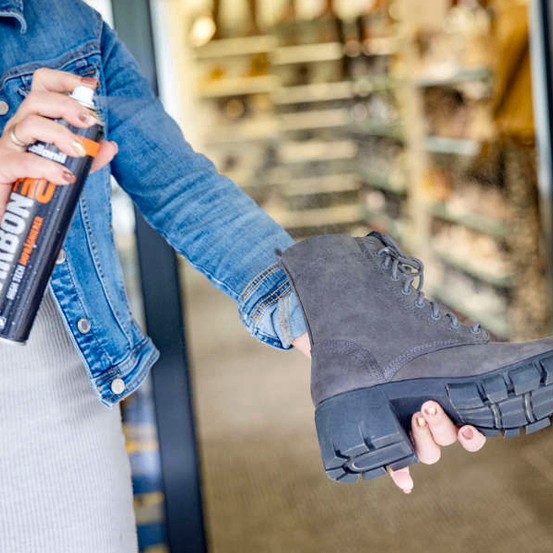 A woman holding a can of Carbon cleaning spray and a grey boot. She is standing in front of a store.