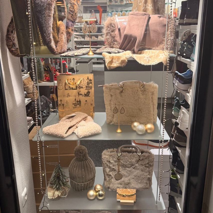 Ein Boutique-Shop-Display mit verschiedenen Winteraccessoires wie Mützen, Handschuhen und Handtaschen, die auf Glasschränken mit dekorativen Elementen und einer Weihnachtskarte angeordnet sind.