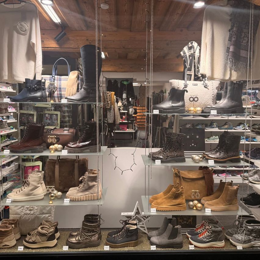 Ein Boutique präsentiert verschiedene Winterstiefel, Taschen und Accessoires. Die Regale sind mit Stiefeln in verschiedenen Stilen und Farben geschmückt, einige mit dekorativen Ornamenten. Die Holzdecke und die Beleuchtung schaffen eine warme Atmosphäre.