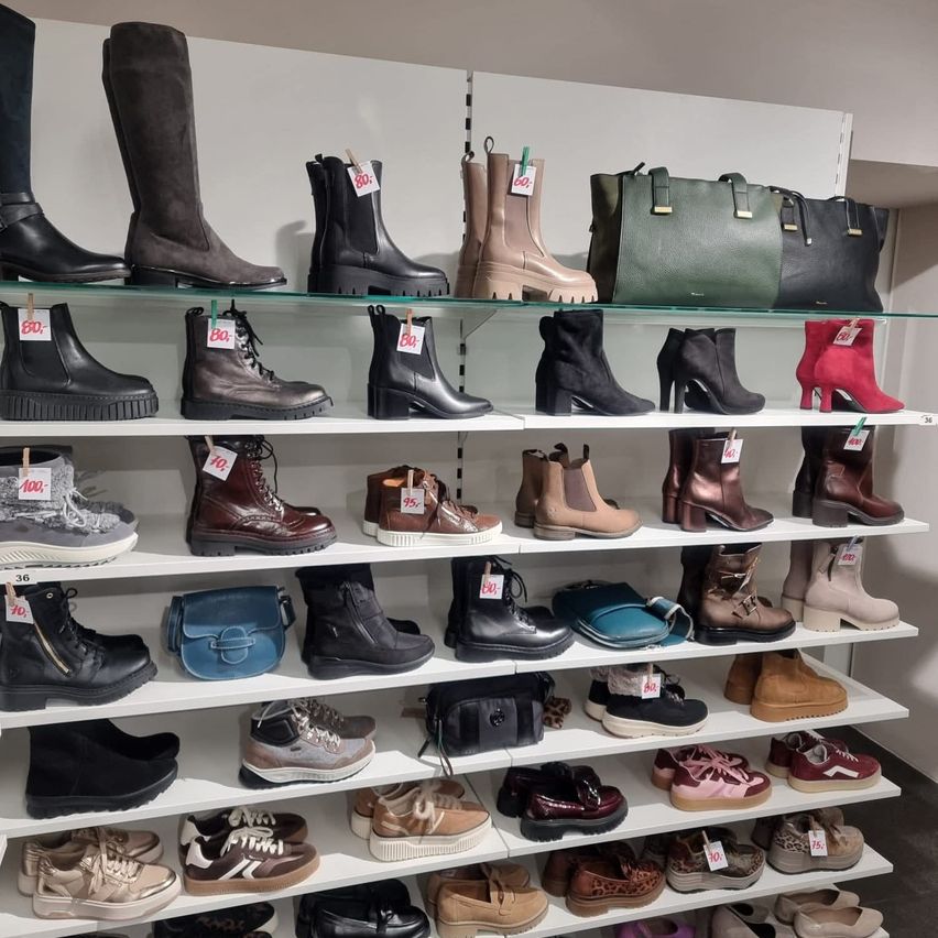 Ein Schuhgeschäft zeigt verschiedene Stiefel, Stiefeletten und Sneakers auf weißen Regalen. Die Preise sind auf den Produkten angegeben.