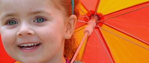 Ein junges Mädchen mit roten Haaren hält einen Regenschirm mit roten und gelben Farbtönen.